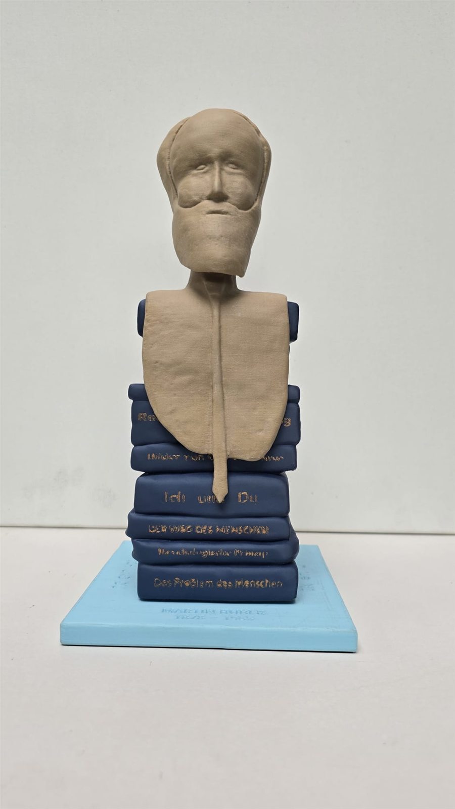 Skulptur von Martin Buber: Büste auf einem Stapel blauer Bücher mit goldenen Titeln